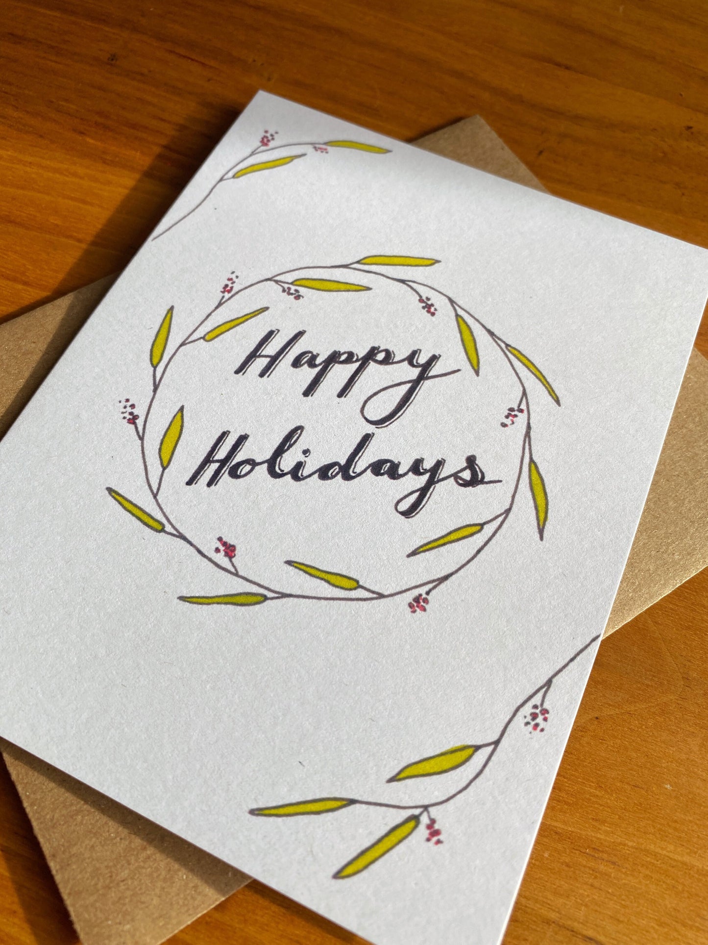 Watercolor greeting card that says "Happy Holidays" with greenery